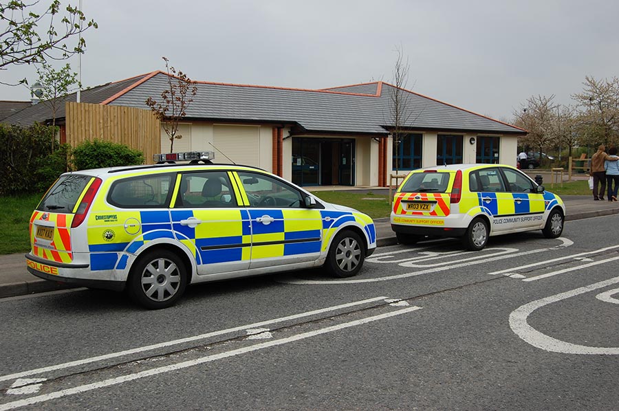 Photo of two police cars parked on a road in front of a community building.