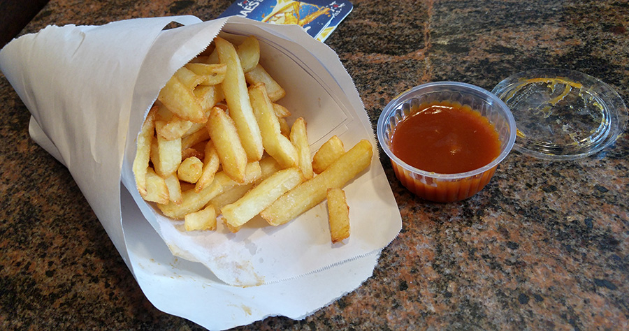 Photo of a bag of takeaway fries and a small dish of ketchup.