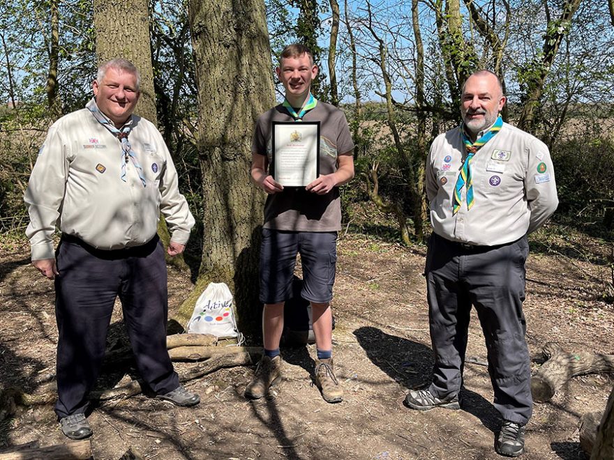 Photo of a Scout holding a certificate flanked by two Scout leaders.