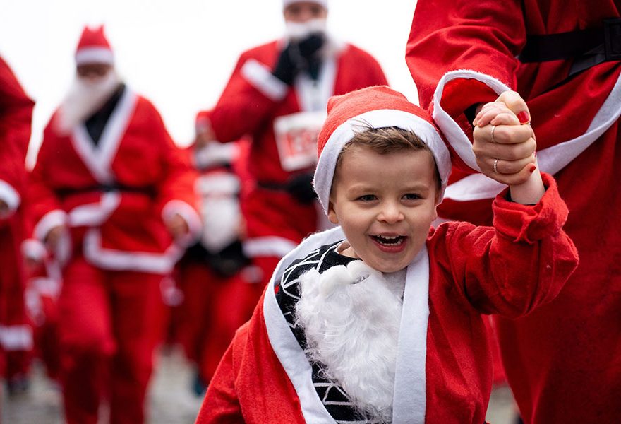 Photo of a child and adults dressed in Santa suits and running.