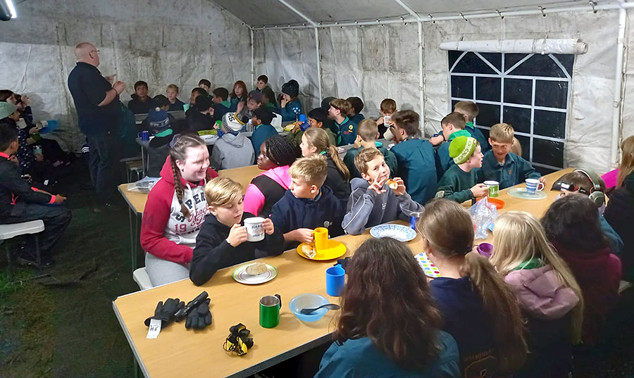Photo of a large group of Scouts sitting at tables inside a marquee.