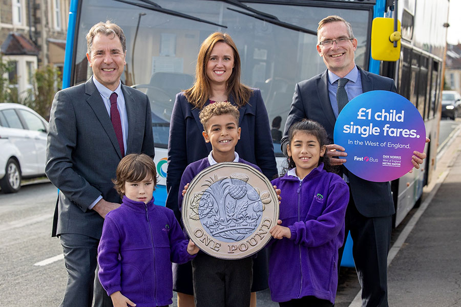 Photo of three adults and three children standing in front of a bus. The children are holding a giant £1 coin.