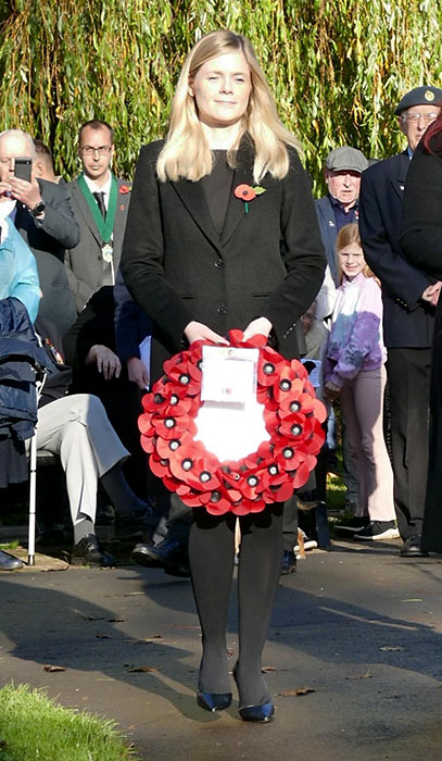 Photo of a woman in a black outfit holding a Remembrance Poppy wreath.