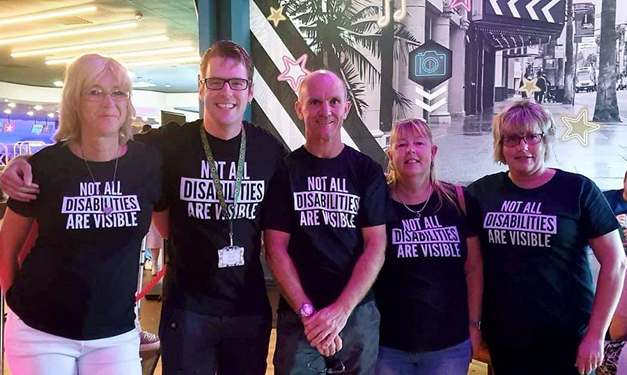 Photo of a group of adults wearing t-shirts emblazoned with the phrase 'Not all disabilities are visible'.