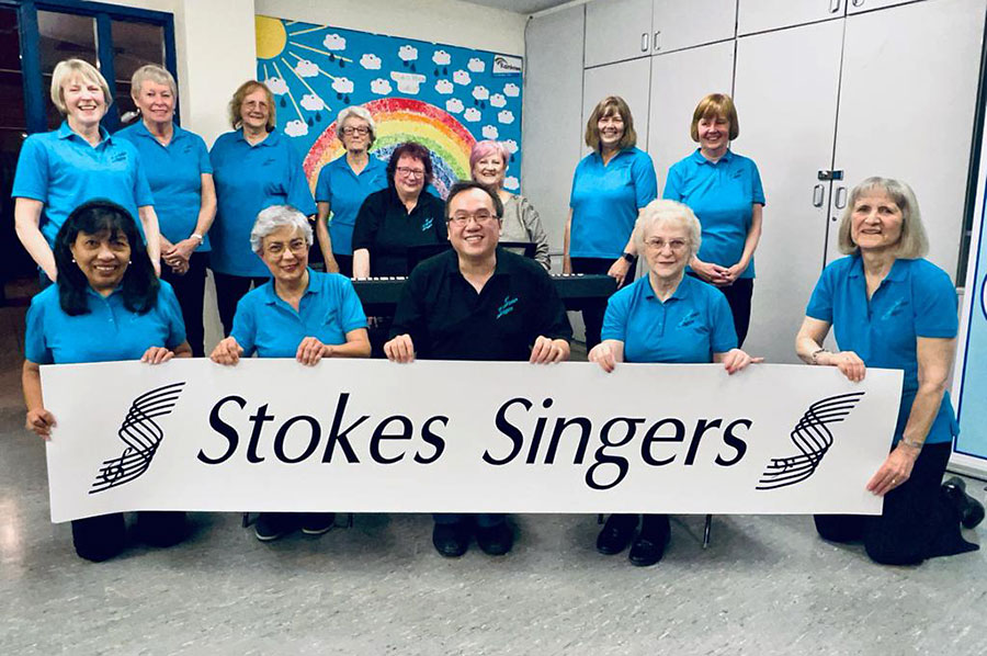 Photo of a group of people holding a banner showing the words 'Stokes Singers'.