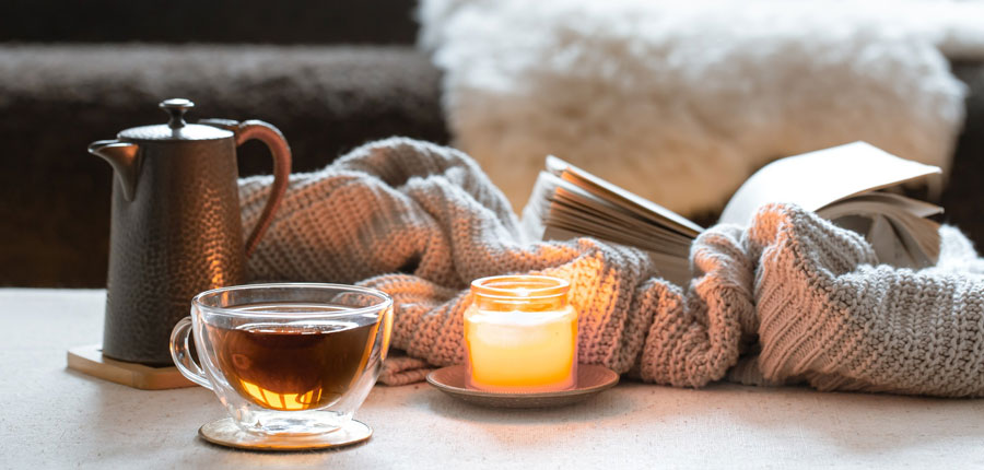 Photo of teapot, glass cup, candle, book and knitted item on a table.