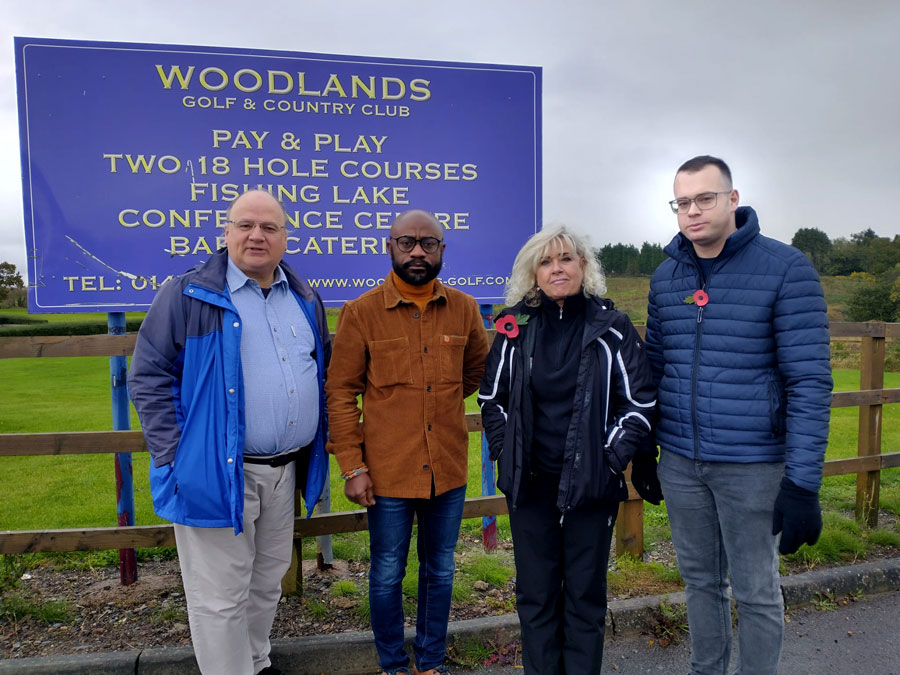 Photo of four people standing in front of a sign promoting a golf course.