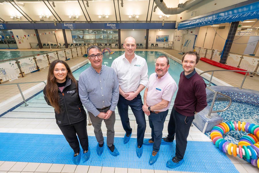 Photo of five people standing in front of an indoor swimming pool.