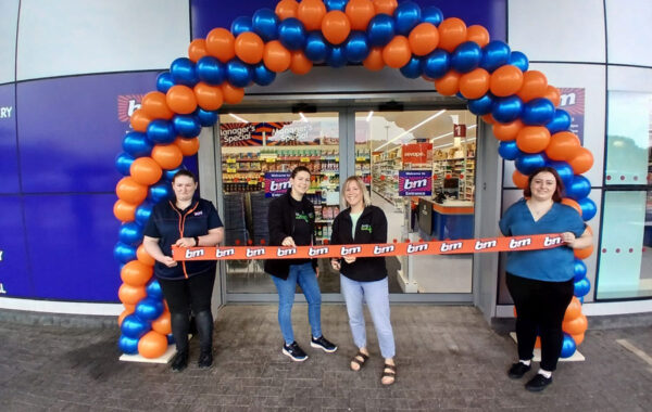 Photo of two people cutting a ribbon in the doorway of a shop.
